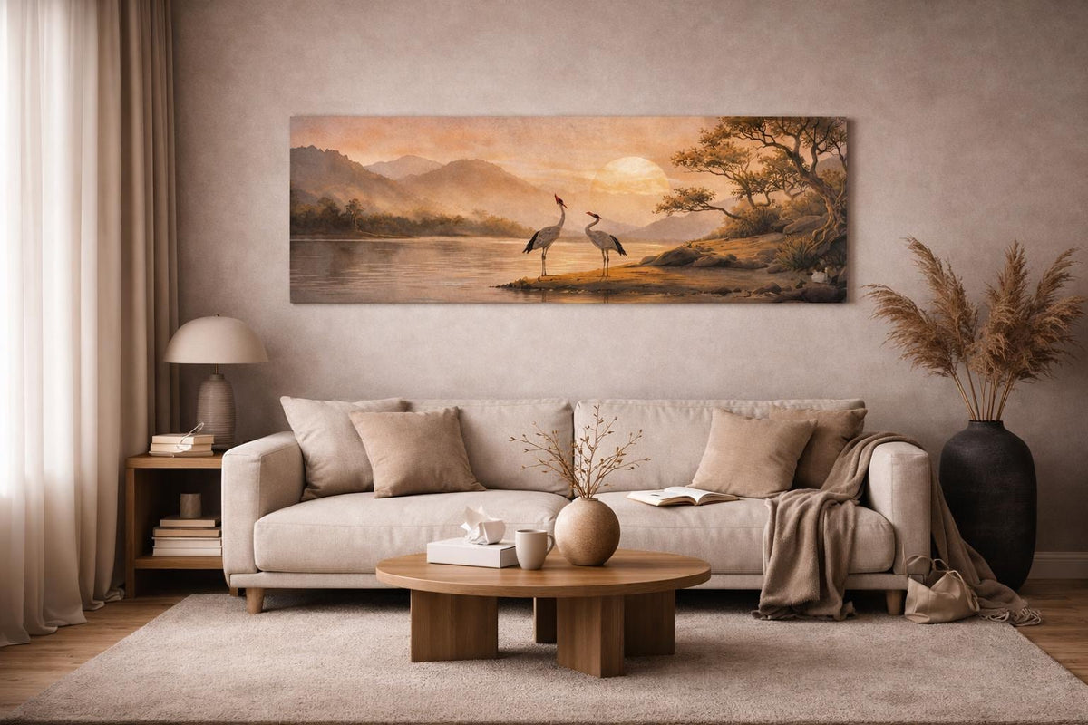 May include: A long, rectangular canvas print showing a tranquil landscape with two cranes by a lake. The artwork uses a warm palette of beige, brown, and orange, with a sunset and mountains in the background. The print is displayed above a beige sofa